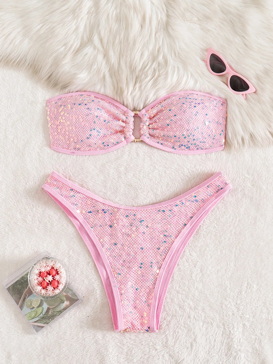 Pink bikini set with floral pattern on a white fur surface, accompanied by sunglasses and a small plant pot.